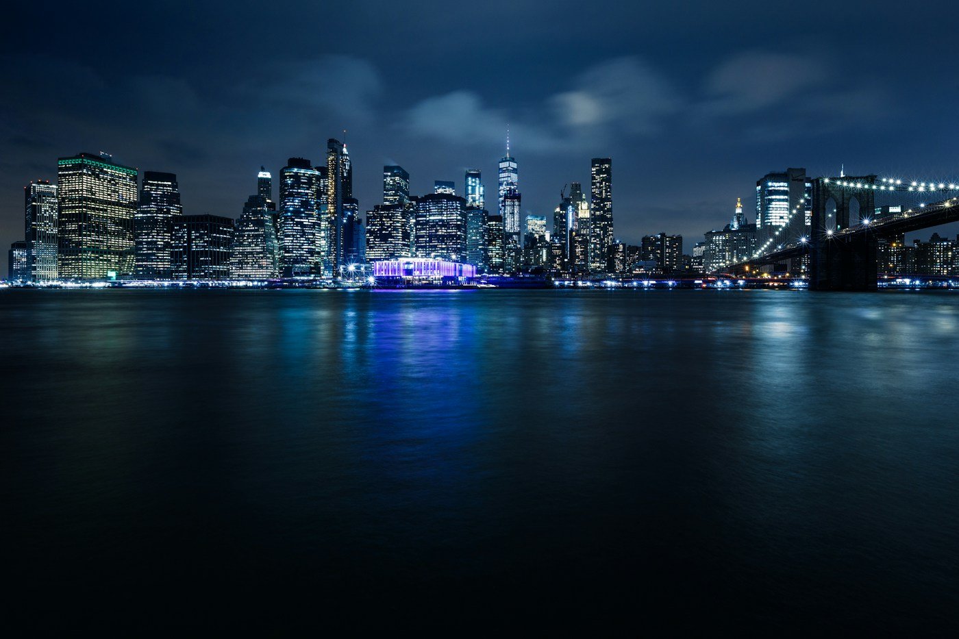Manhattan skyline and Brooklyn Bridge illuminated above the East River at dusk